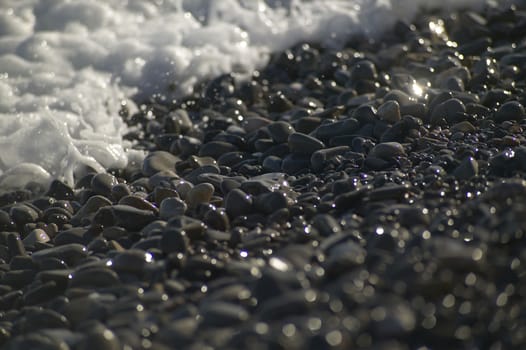 A small detail of the pebbles on a beach hit by the sea waves crashing shore.