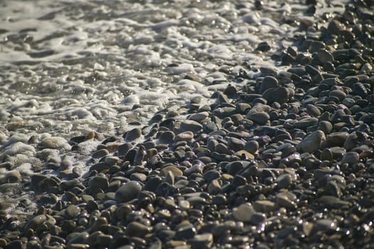 A small detail of the pebbles on a beach hit by the sea waves crashing shore.