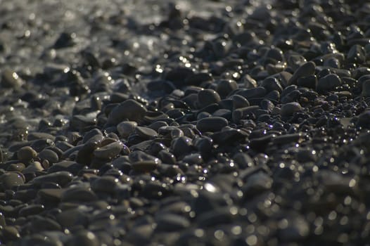A small detail of the pebbles on a beach hit by the sea waves crashing shore.