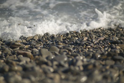 Sea water, wave blowing over the rocks of Nice Beach in France, letting the water splashing out into the air.