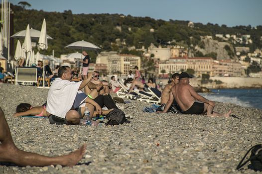 Daily life scene on the beach of Nice, with fun and relaxed tourists who enjoy their relaxing time kissed by the sun of the twilight.