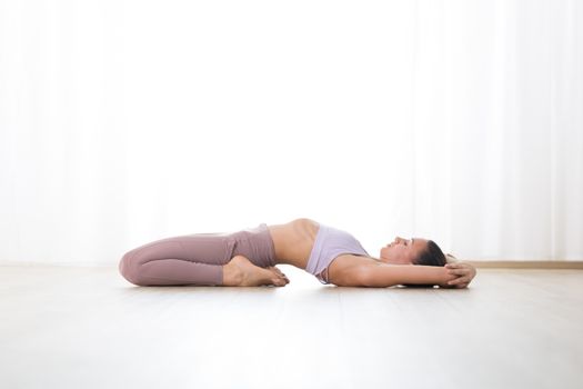 Portrait of gorgeous active sporty young woman practicing yoga in studio. Beautiful girl practice Supta Vajrasana, fixed firm yoga pose. Healthy active lifestyle, working out indoors in gym.