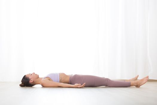 Portrait of gorgeous active sporty young woman practicing yoga in studio. Beautiful girl relaxing in Savasana, corpse pose. Healthy active lifestyle, working out indoors in gym.