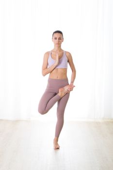 Portrait of gorgeous active sporty young woman practicing yoga in studio. Beautiful girl practice Tadasana, tree yoga pose. Healthy active lifestyle, working out indoors in gym.