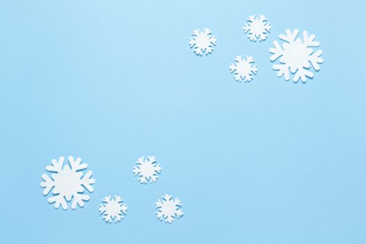 Christmas composition, group of little white felt snowflakes on pastel blue background, copy space. Festive, New Year concept. Horizontal, flat lay. Minimal style. Top view.