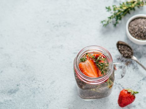 View from above chia water in mason jar with strawberry and thyme on gray cement background. Chia infused detox water with berries. Copy space for text. Healthy eating, drinks, diet, detox concept