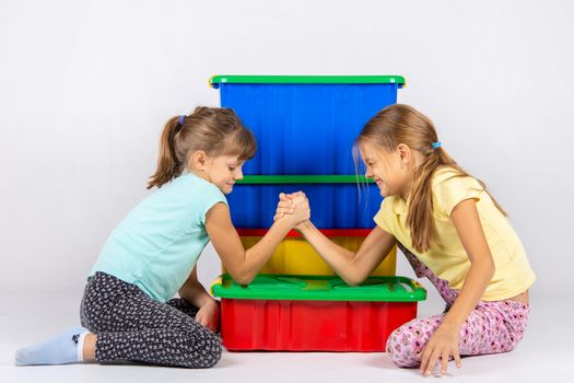 Two girls fight on hands, putting elbows on a box with toys