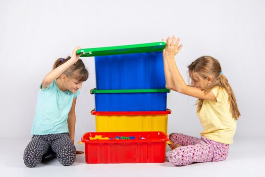 Two girls opened the lid of a large plastic box with toys, and look inside