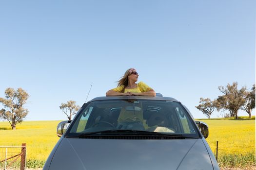 Beautiful woman standing in the sunroof of her car on a road trip to countrysideBeautiful woman standing in the sunroof of her car on a road trip to countryside and rural farm fields