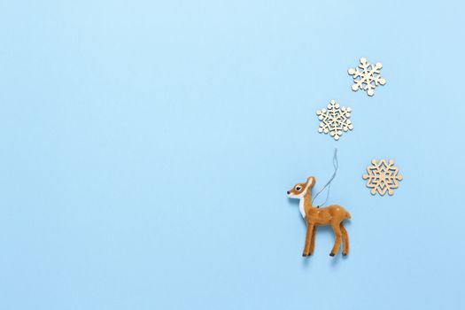 Christmas decoration, naturalistic toy roe deer and three little wooden snowflakes on pastel blue background, copy space. Festive, New Year concept. Horizontal, flat lay. Minimal style. Top view.