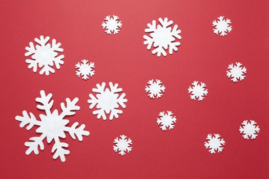 Christmas composition, group of big and small white felt snowflakes on burgundy red background. Festive, New Year concept. Horizontal, flat lay. Minimal style. Top view.