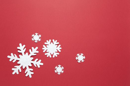 Christmas composition, group of big and small white felt snowflakes on burgundy red background, copy space. Festive, New Year concept. Horizontal, flat lay. Minimal style. Top view.