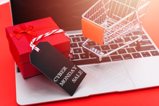 Internet online shopping marketing, top view of workspace with Cyber Mondat text black tag, gift box and cart shopping on laptop computer on red background and have copy space for use