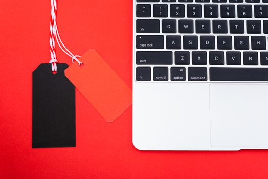 Internet online shopping marketing, top view of workspace with Blank red and black tags near laptop computer on red background