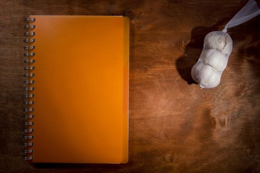 Garlic heads and orange notebook on a wooden table
