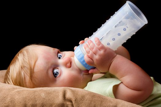 A little guy is drinking from his milk bottle very heavily. Even has a little milk drool coming out.