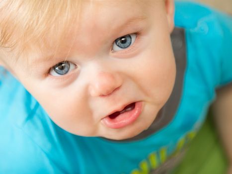 A little toddler boy is making a very sad face up at the camera. depth of field is very shallow and focused on the eyes.