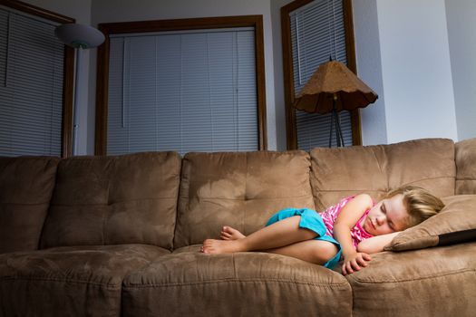 Child on couch curled up into a little ball at night. Nice warm light is on child that falls off as it moves away