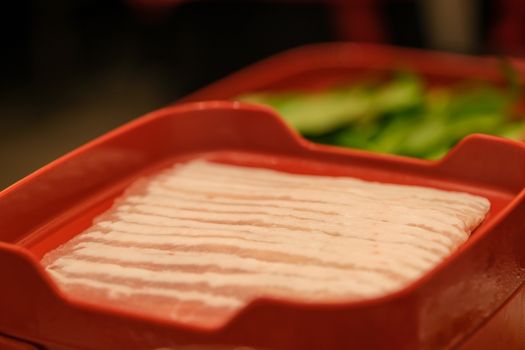 The sliced raw pork meat isolated on a red plate background. Top view.