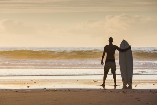 Surfer on the beach holding is surfboard and checking the waves