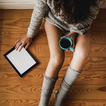 Woman sitting on the floor drinking a coffee and using a tablet 