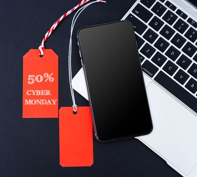 Online shopping Cyber Monday sale 50% text on red tag and blank tag near smart phone and laptop computer with black background
