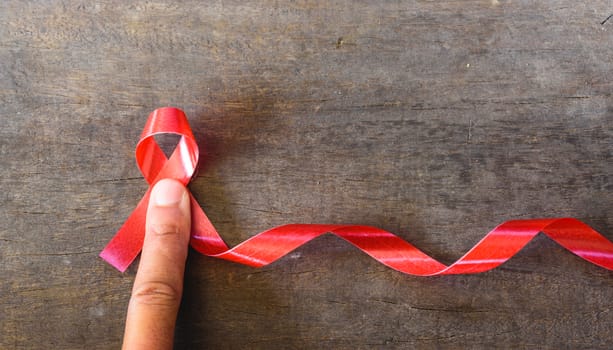 Red Ribbon Support HIV, AIDS and have finger on wooden background and copy space for use