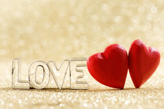 Two red handmade wooden hearts and word love on golden bright glitter lights bokeh background