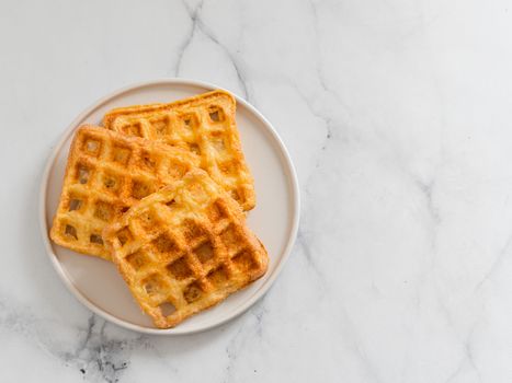Delicious savory keto waffles. Two ingredients chaffles on plate over white marble background. Eggs and parmesan cheese low carb waffles. Top view or flat lay. Copy space right for text or design.