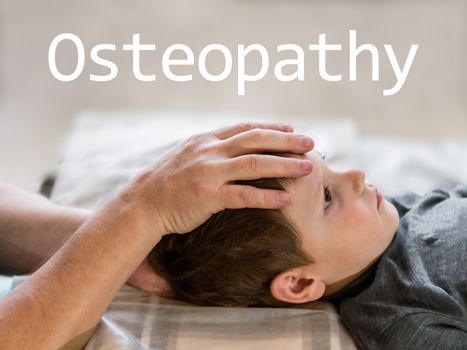 Osteopathy Treatment and word Osteopathy. Elementary age boy's forehead being manipulated by real osteopathic physician