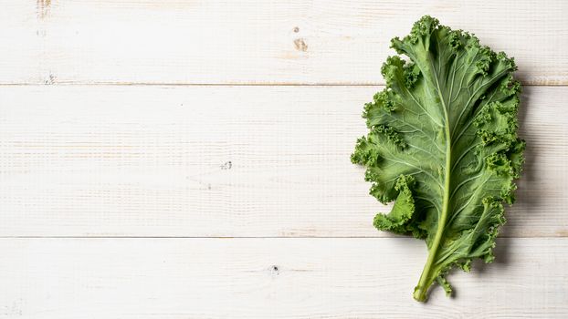 Fresh green kale leaf on white wooden tabletop. Healthy detox vegetables. Vegetarian food, healthy eating, dieting concept. Top view or flat lay. Copy space. Health kale benefits. Banner