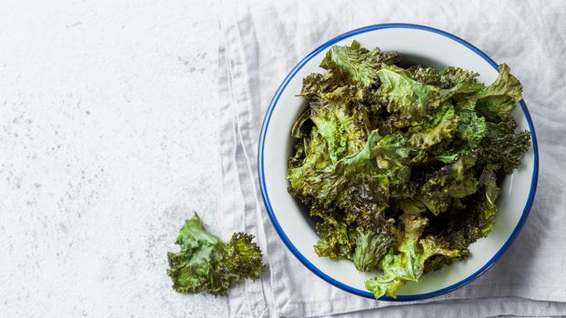 Green Kale Chips with salt on plate. Homemade healthy snack for low carb, keto, low calorie diet. Gray cement background. Ready-to-eat kale chips, copy space for text. Top view or flat lay. Banner