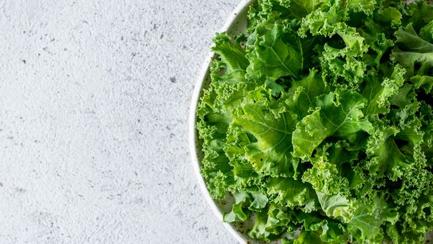 Kale close up. Green vegetable leaves, top view in white craft bowl over gray cement background. Healthy eating, vegetarian food,dieting concept. Top view or flat lay. Copy space. Health kale benefits