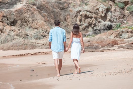 Happy couple walking on sand of tropical beach