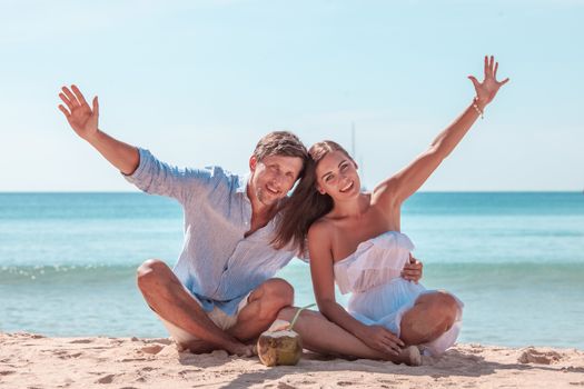 Happy smiling couple sitting on beach with raised arms