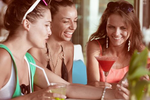 Three friends amazed watching a smart phone sitting in cafe drinking cocktails