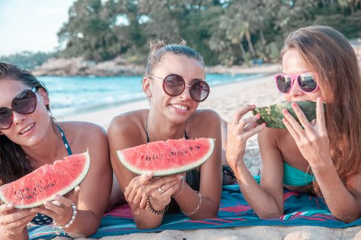 Happy smiling female friends eating watermelon on beach