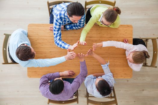 Coworkers doing high five sitting at the office table, top view