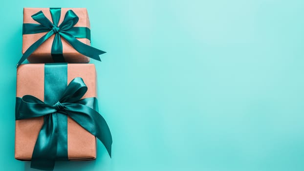Two gift boxes in craft wrapping paper and green satin ribbon on turquoise blue background, copy space right. Beautiful Christmas, New Year or Birthday presents, flat lay or top view. Banner
