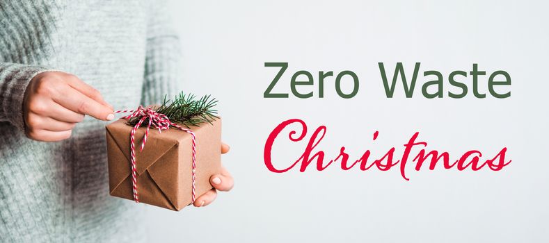Zero waste Christmas concept. Female hands opening gift box in craft wrapping paper. Free font letters Zero Waste Christmas.