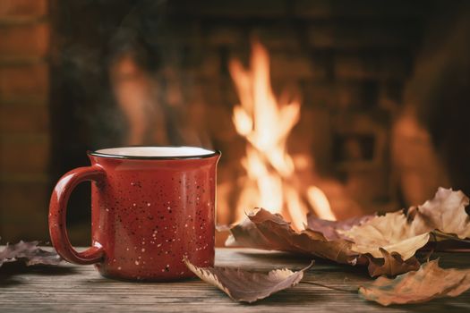 Red mug with hot tea in front of a burning fireplace, comfort and warmth of the hearth concept.