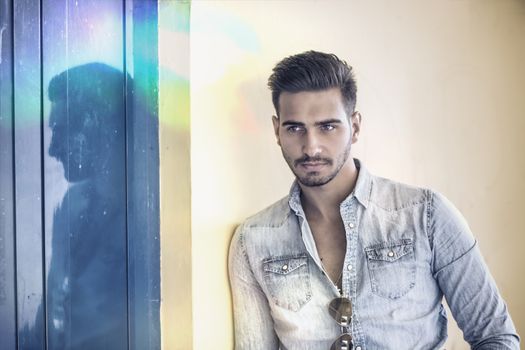 Attractive young man standing against colorful wall, looking at camera, wearing denim shirt