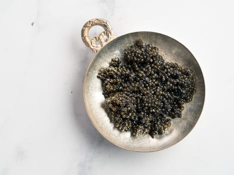 Black caviar top view or flat lay. Bowl of black caviar on white marble background. Copy space for text.
