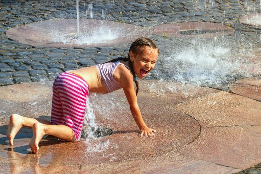 Girl on a sunny summer day are poured water from a fountain.Girl happily in shallow clean water on of city fountain on warm bright summer day.