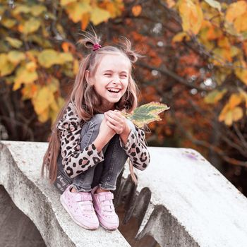 Girl holding colorful leaf in autumn park.