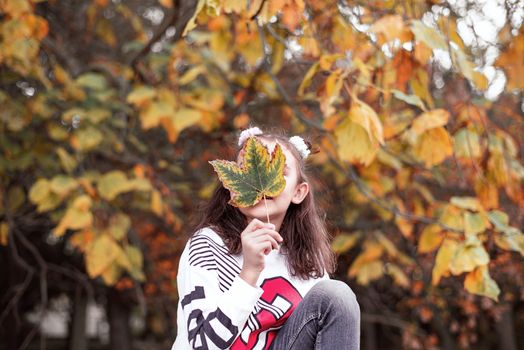 Girl holding colorful leaf in autumn park.