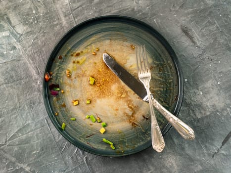 Dirty dish and silverware cutlery on gray background, top view or flat lay. Empty dirty craft plate with fork and knife on gray textured background.