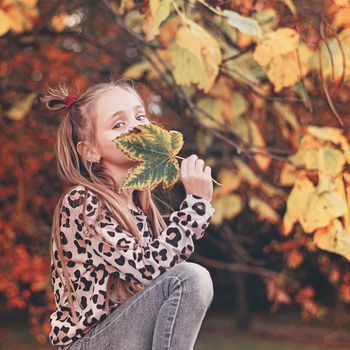 Girl holding colorful leaf in autumn park.