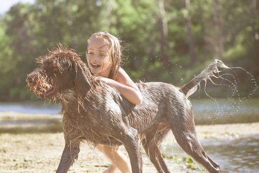 Little girl playing in the river with a dog on a summer sunny day.The concept of playing with a dog in nature and walking on the beach with Pets.Little girl playing with dog.