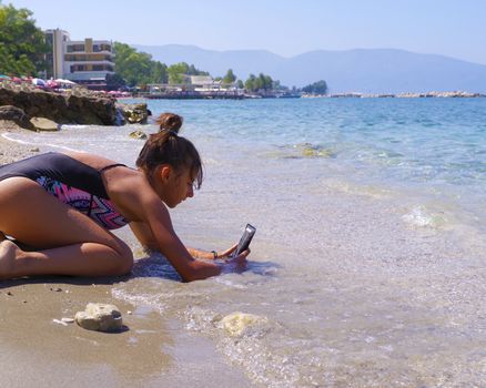 Summer season. Sea and beach.Young beautiful girl sits on a beach near the sea and takes pictures on the phone.